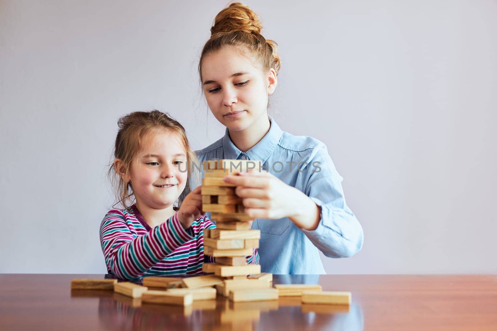 Little girl preschooler and her elder sister playing together with wooden blocks game toy. Siblings spending time sitting at desk at home