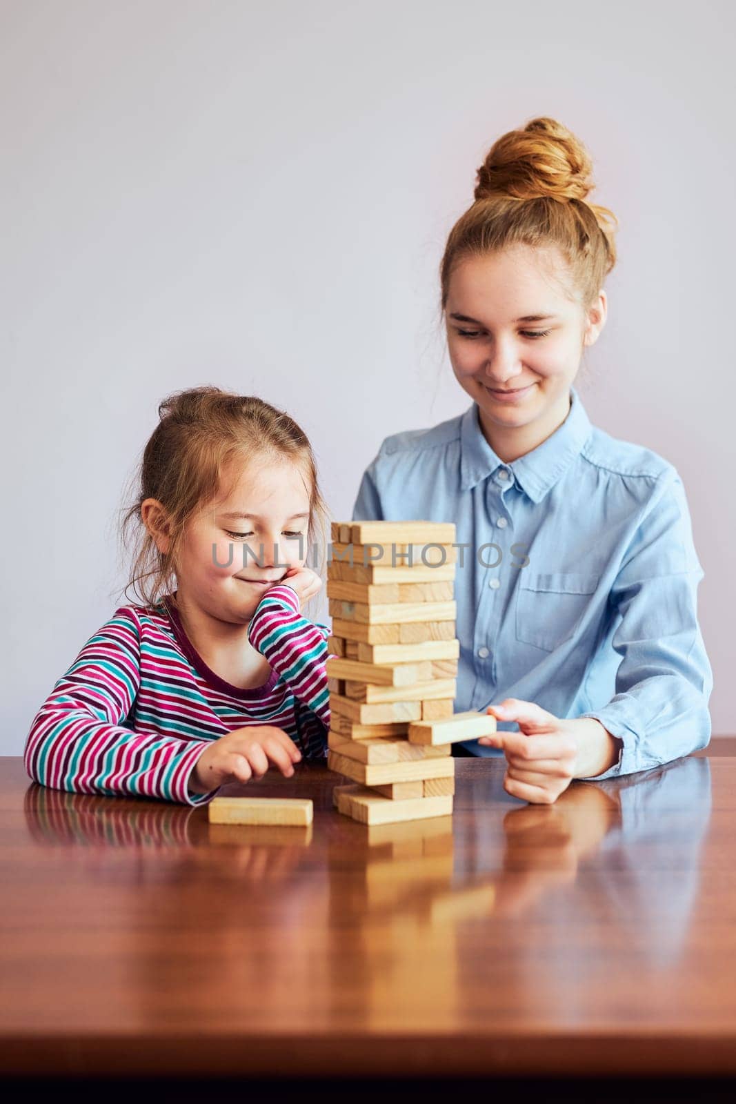 Little girl preschooler and her elder sister playing together with wooden blocks game toy. Siblings spending time sitting at desk at home