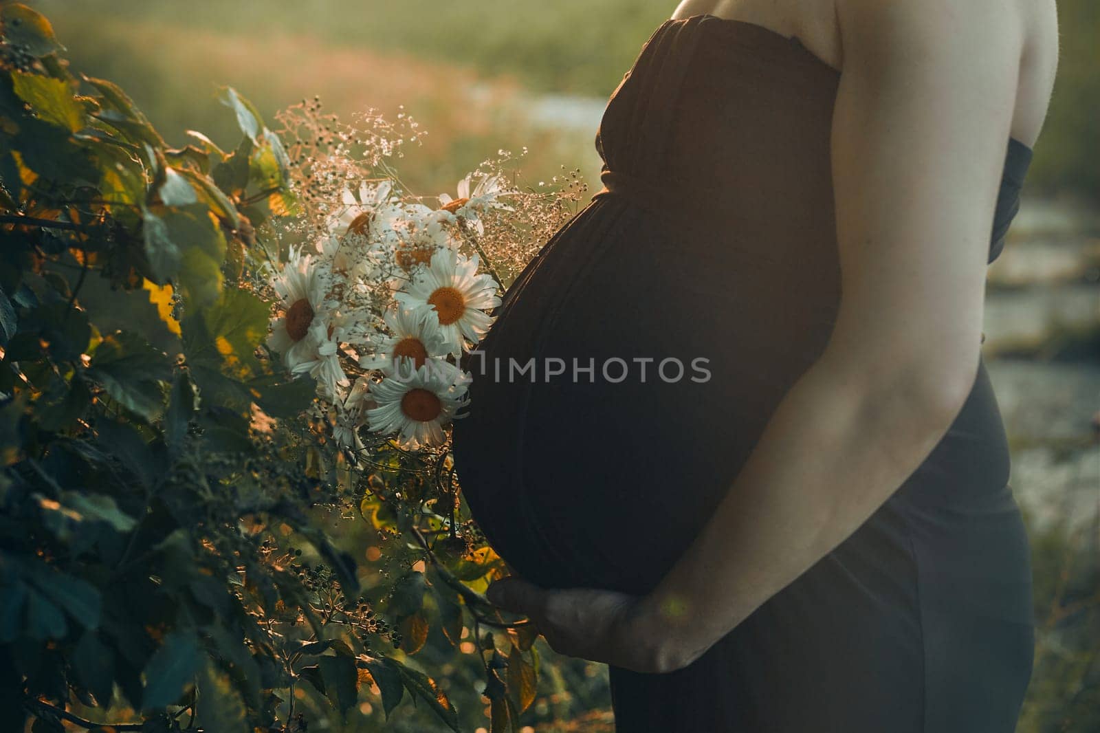 Pregnant woman hugging her tummy standing outdoors surrounded by nature. Pregnancy, expectation, motherhood concept