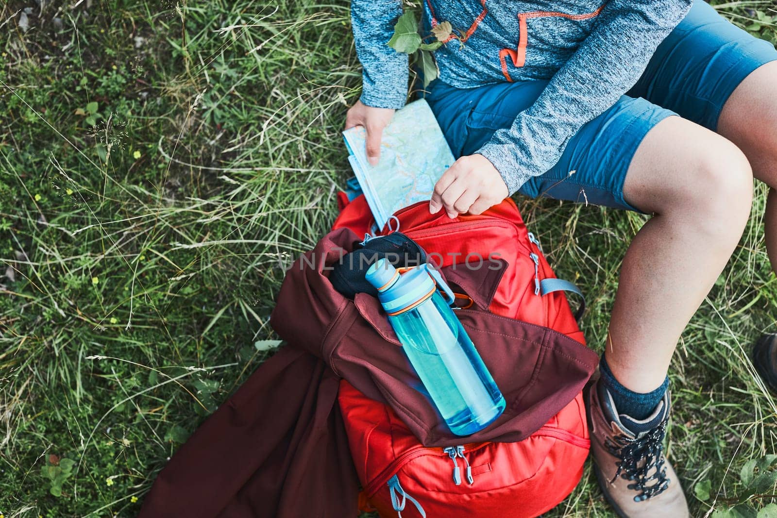 Woman with backpack having break during trip in mountains taking map out sitting on grass on summer vacation day