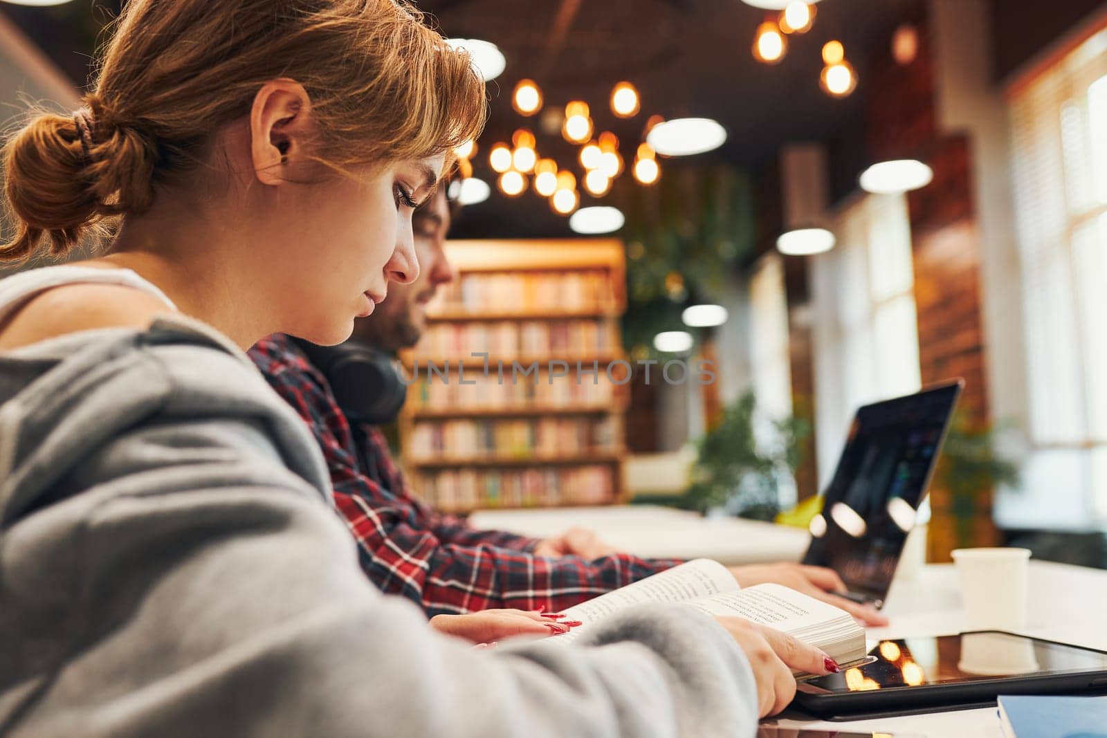 Students learning in university library. Young man preparing for test on laptop. Girl learning from book. Focused students studying for college exams. Students discussing and learning together sitting at desk. Back to school