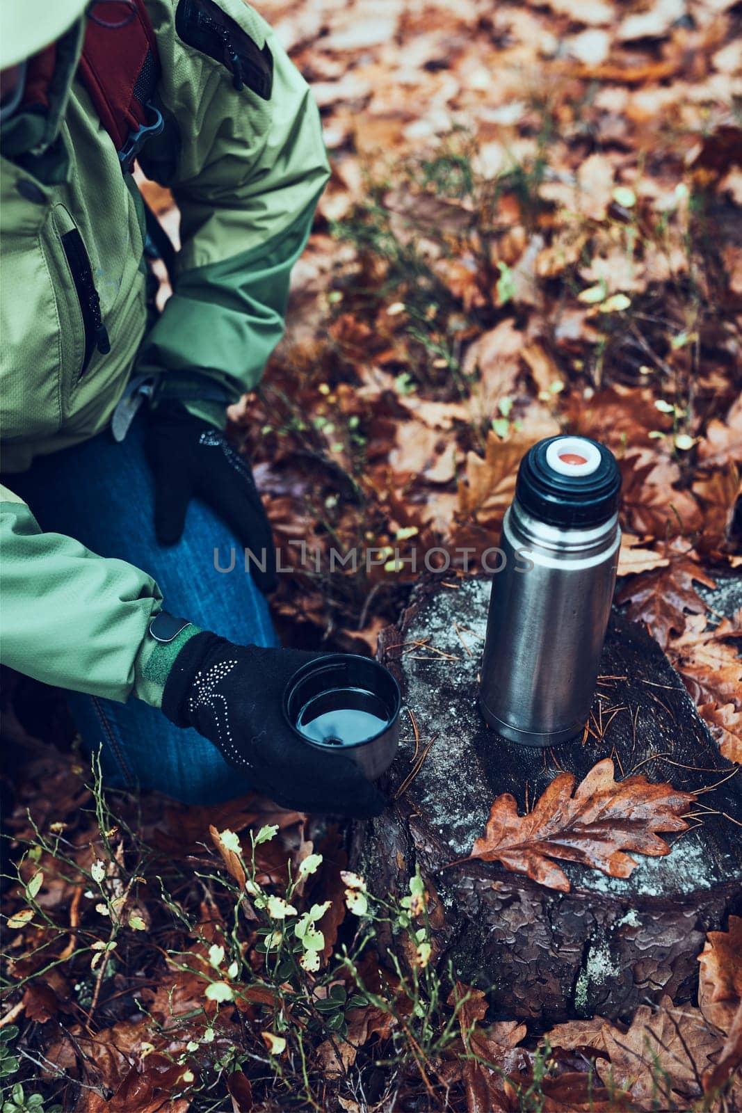 Woman with backpack having break during trip on autumn cold day drinking a hot drink from thermos flask. Active middle age woman wandering around a forest actively spending time