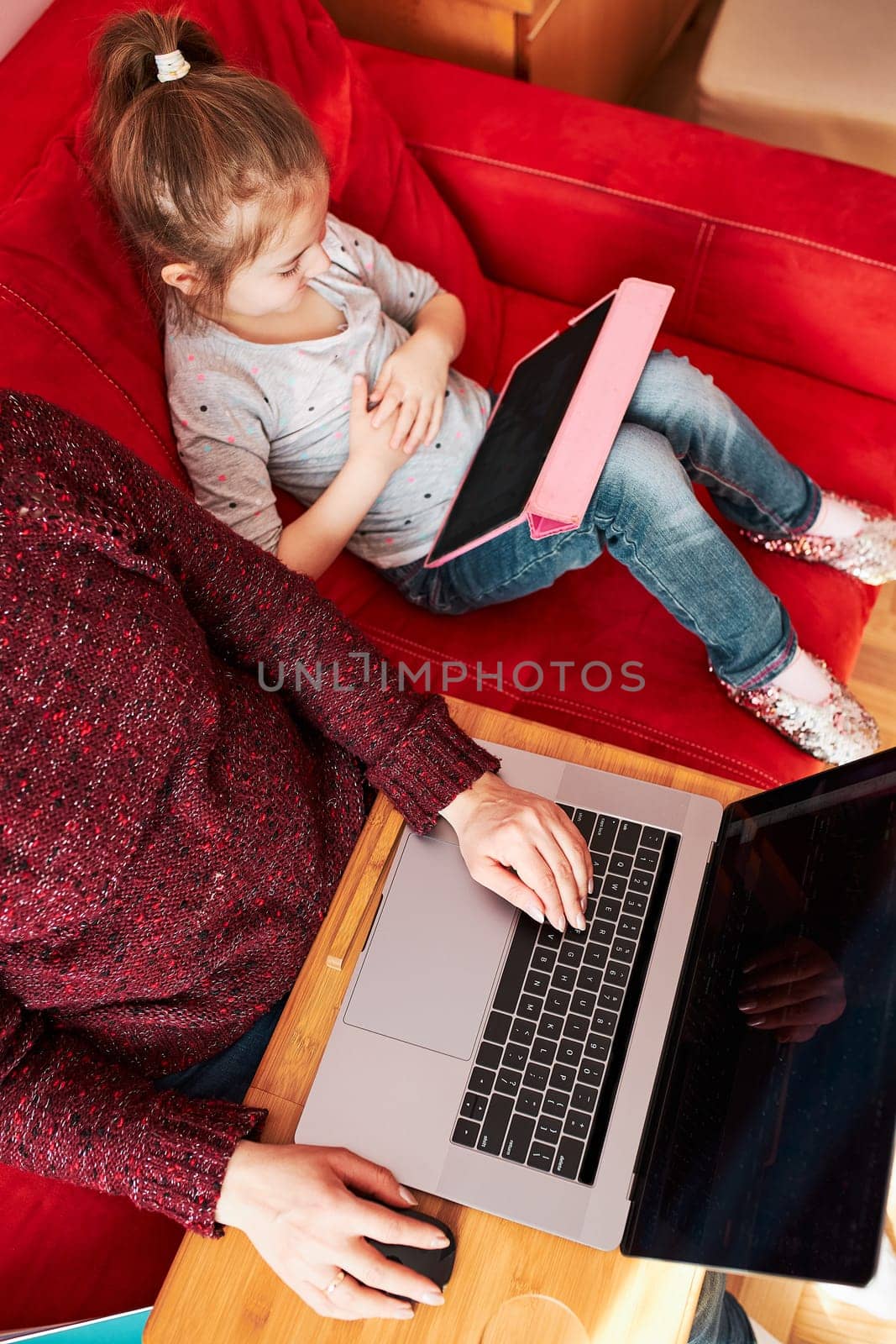 Woman mother working doing her job remotely during video chat call stream online course webinar on laptop from home during COVID-19 quarantine while her daughter watching video on tablet. Woman sitting on bed in front of computer looking at screen