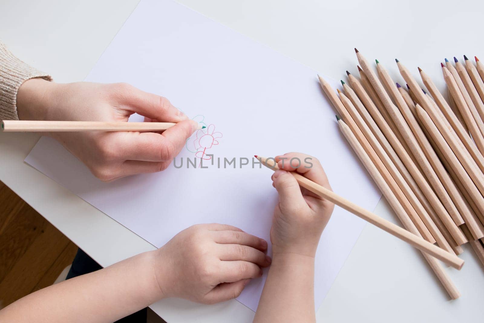 Child and adult drawing together with colored pencils on white paper.