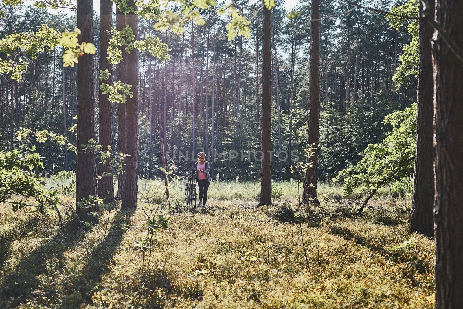 Active woman cycling on forest road. Female riding bicycle off-road route on summer vacation day. Woman wearing bicycle helmet and gloves