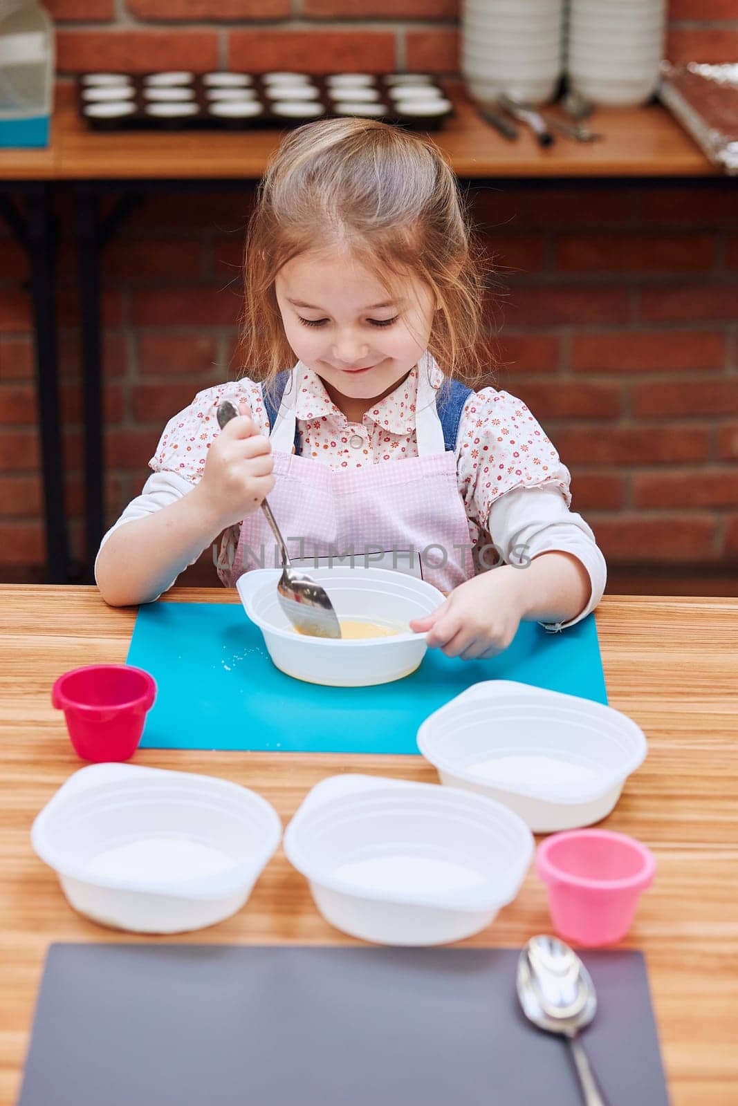 Happy, smiling little girl stirring the yolk with sugar. Kid taking part in baking workshop. Baking classes for children, aspiring little chefs. Learning to cook. Combining and stirring prepared ingredients. Real people, authentic situations