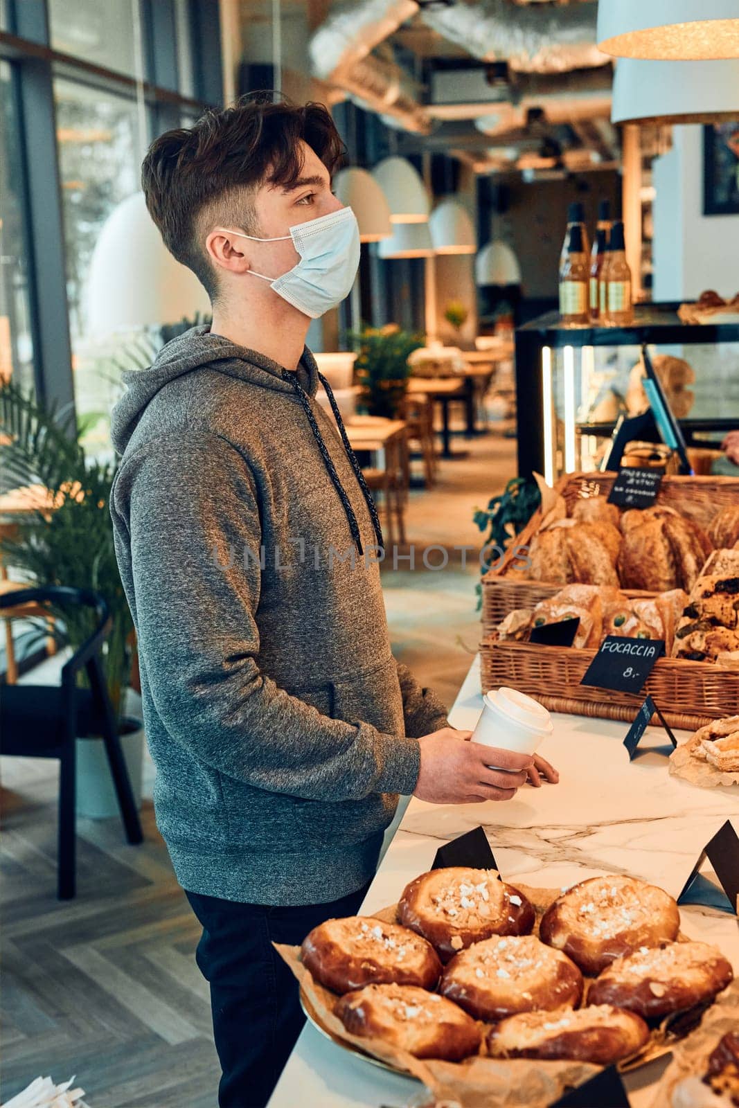 Man buying coffee and cake in the coffee shop to go. Man standing at counter wearing the face mask to avoid virus infection and to prevent the spread of disease in time of coronavirus