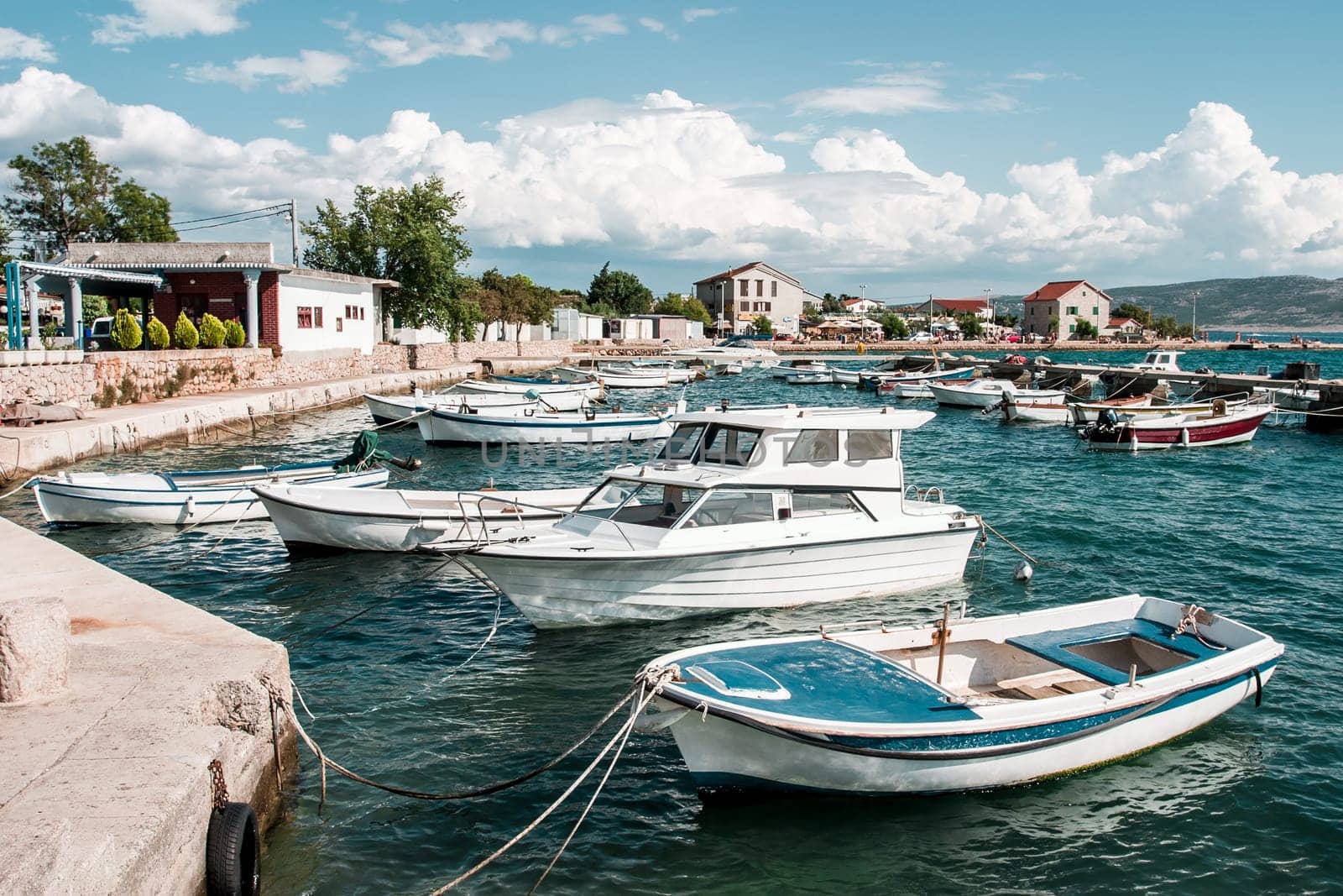 Many boats moored to the pier and shore. Town in the distant