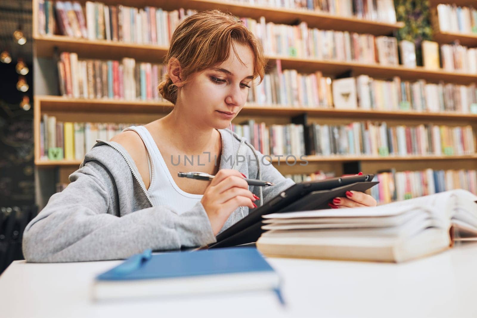 Student learning in university library. Young woman writing essay and making notes using computer tablet. Focused student studying for college exams. Using technology. Back to school