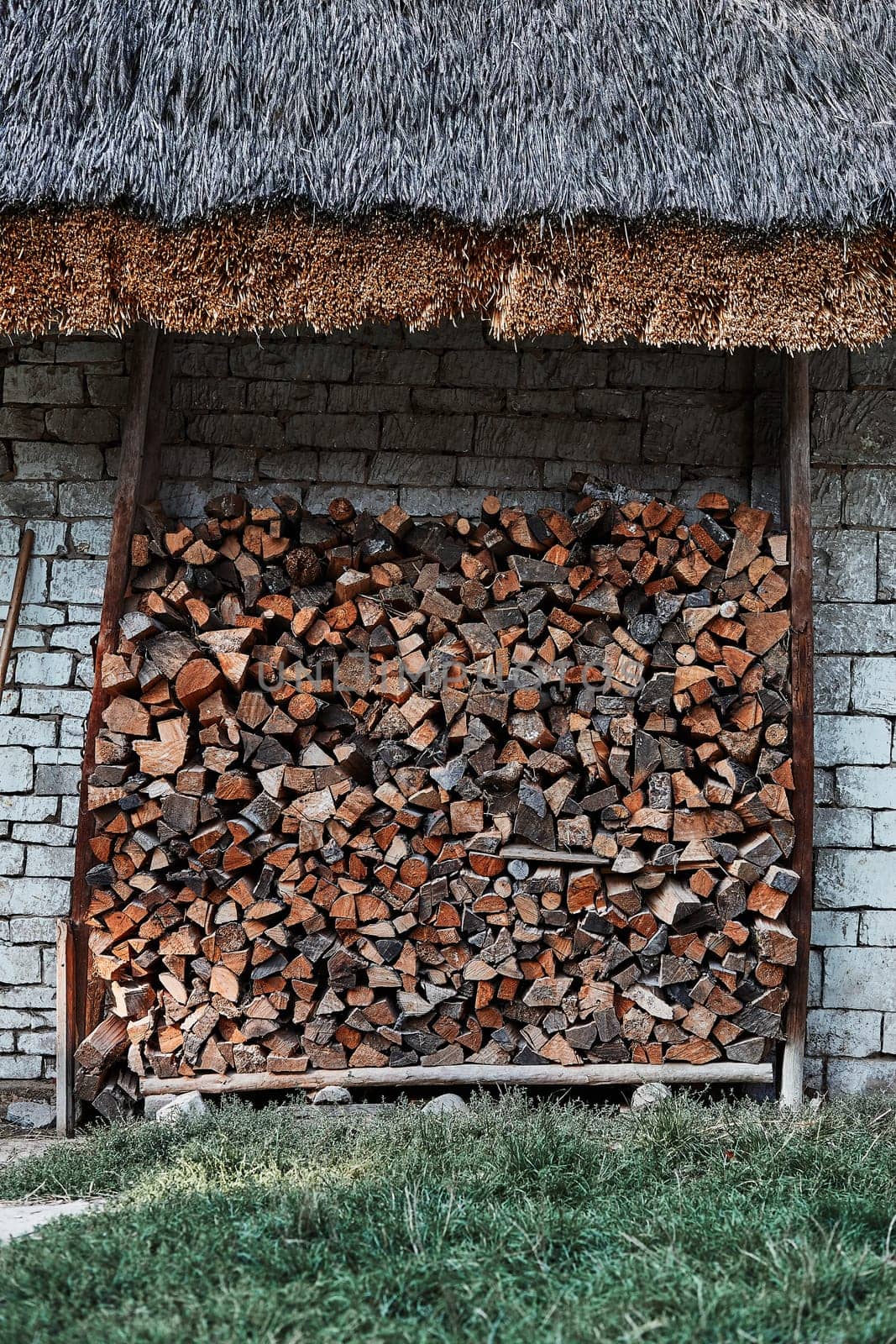 Logs of firewood stored under the stone shed. Stacked firewood in a backyard back of house