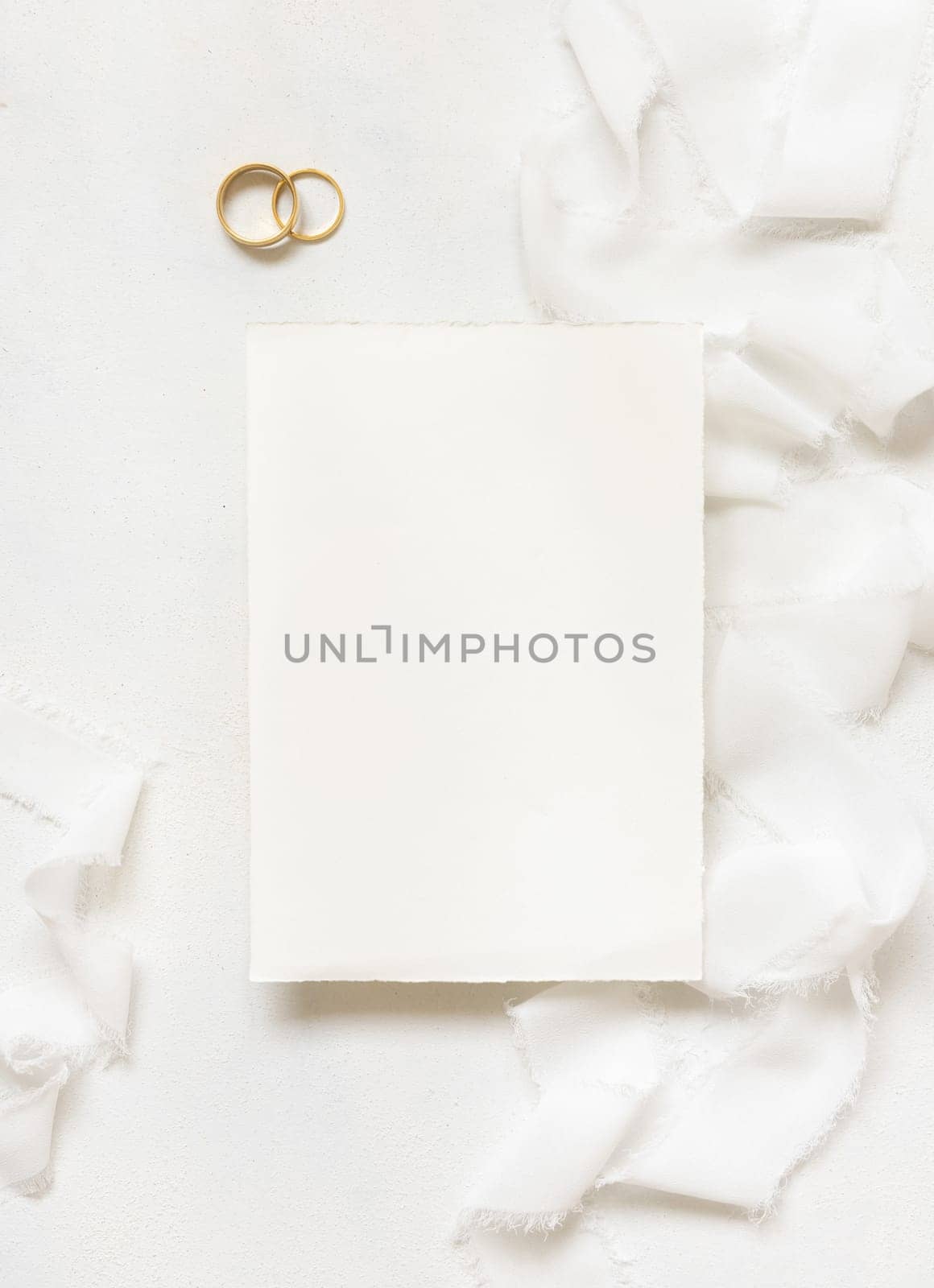 Blank card near white silk ribbons and wedding rings top view, wedding mockup. Romantic scene with vertical card and pastel flowers flat lay. Valentines, Spring or Mothers day concept