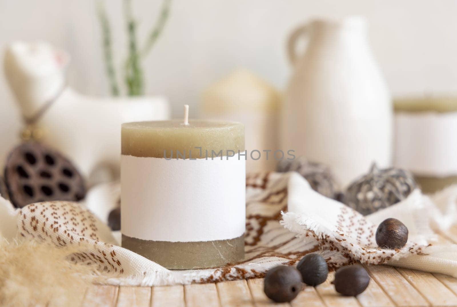 Candle with blank paper label on wooden table near natural decor Close up, copy space. Boho or ethnic packaging mock up. Home decorations in Bohemian or scandinavian style