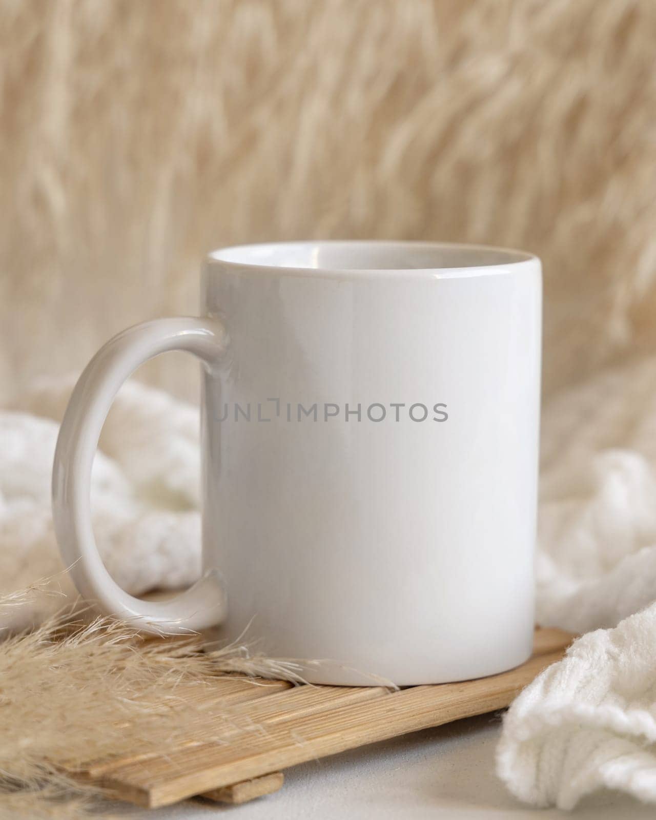 White coffee mug on wooden tray near dry pampas grass and cosy knitted sweater Close up, copy space. Boho packaging mock up. Comfort Bohemian, ethnic or scandinavian style.
