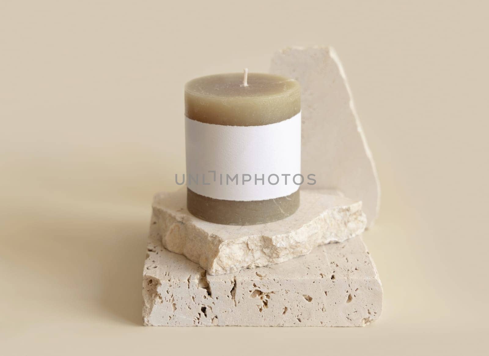 Candle with label on beige near cream travertine stones, Close up, copy space. Brand packaging mock up. Home decoration, minimal interior, Bohemian or scandinavian style