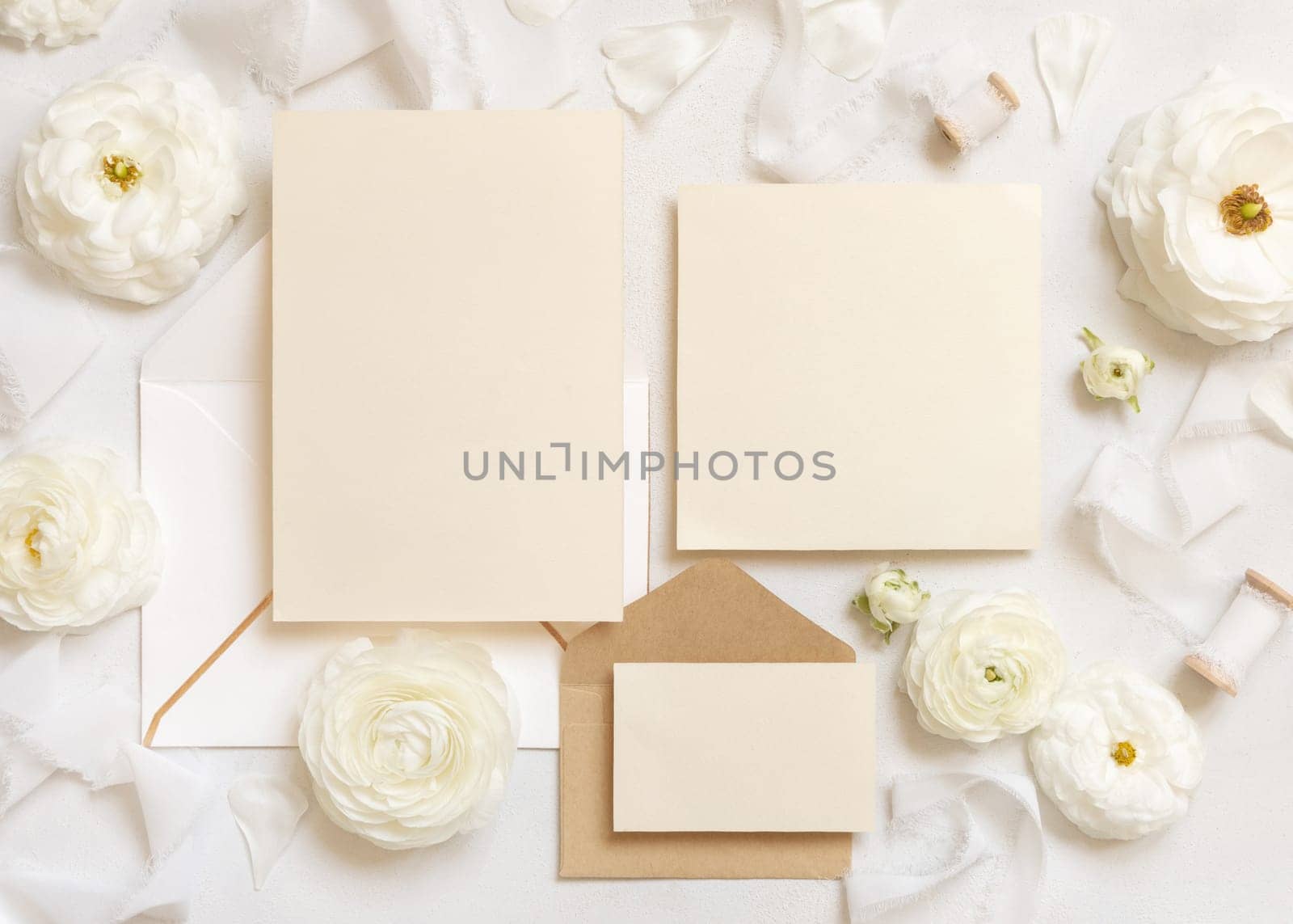 Blank cards and envelopes near cream roses and white silk ribbons top view, mockup. Romantic scene with wedding set and pastel flowers flat lay. Valentines, Spring or Mothers day concept