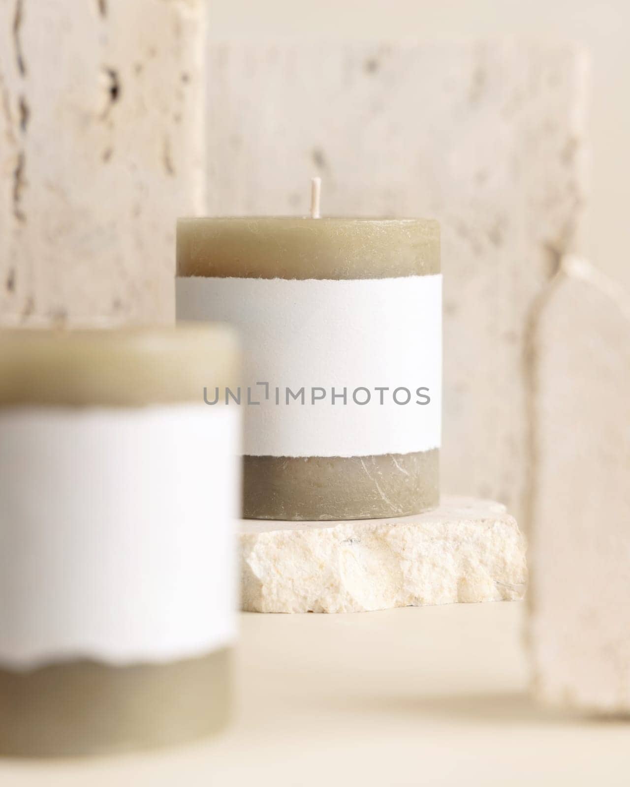 Candles with label on beige near cream travertine stones, Close up, copy space. Brand packaging mock up. Home decoration, minimal interior, Bohemian or scandinavian style
