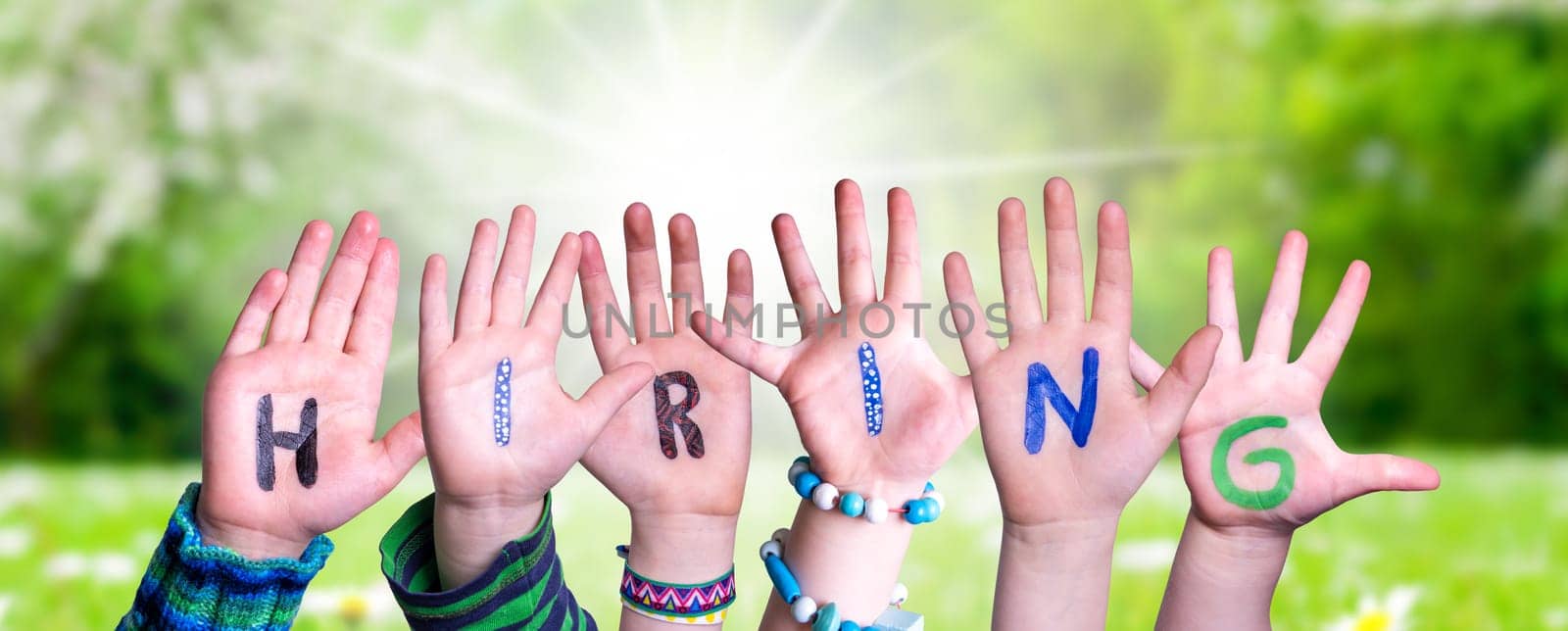 Children Hands Building Colorful English Word Hiring. Sunny Green Grass Meadow As Background.
