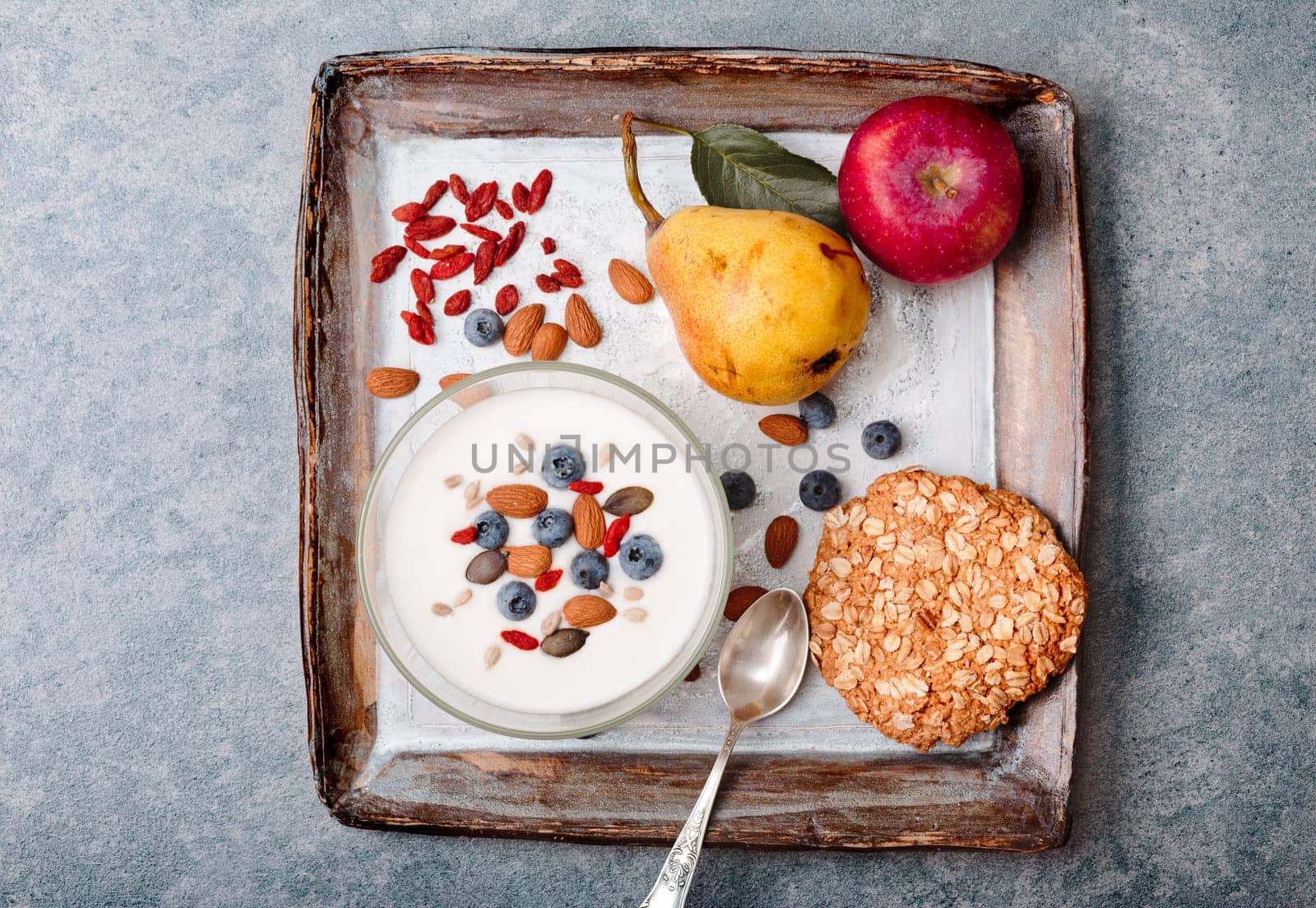 Breakfast on table. Yogurt with added blueberries and roasted almonds. Muesli cookie, apples and pears on table. Light and healthy meal. Good quality balanced diet. Flat top-down composition