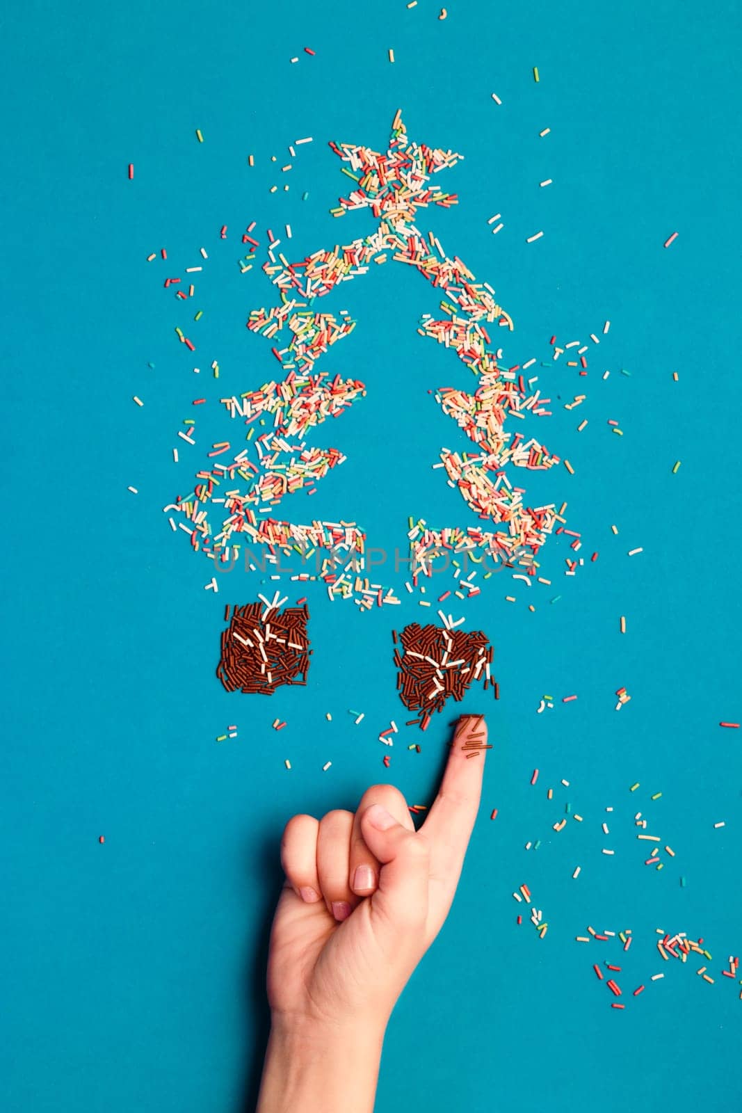 Symbols of christmas tree and gifts made of colored sprinkles on blue background