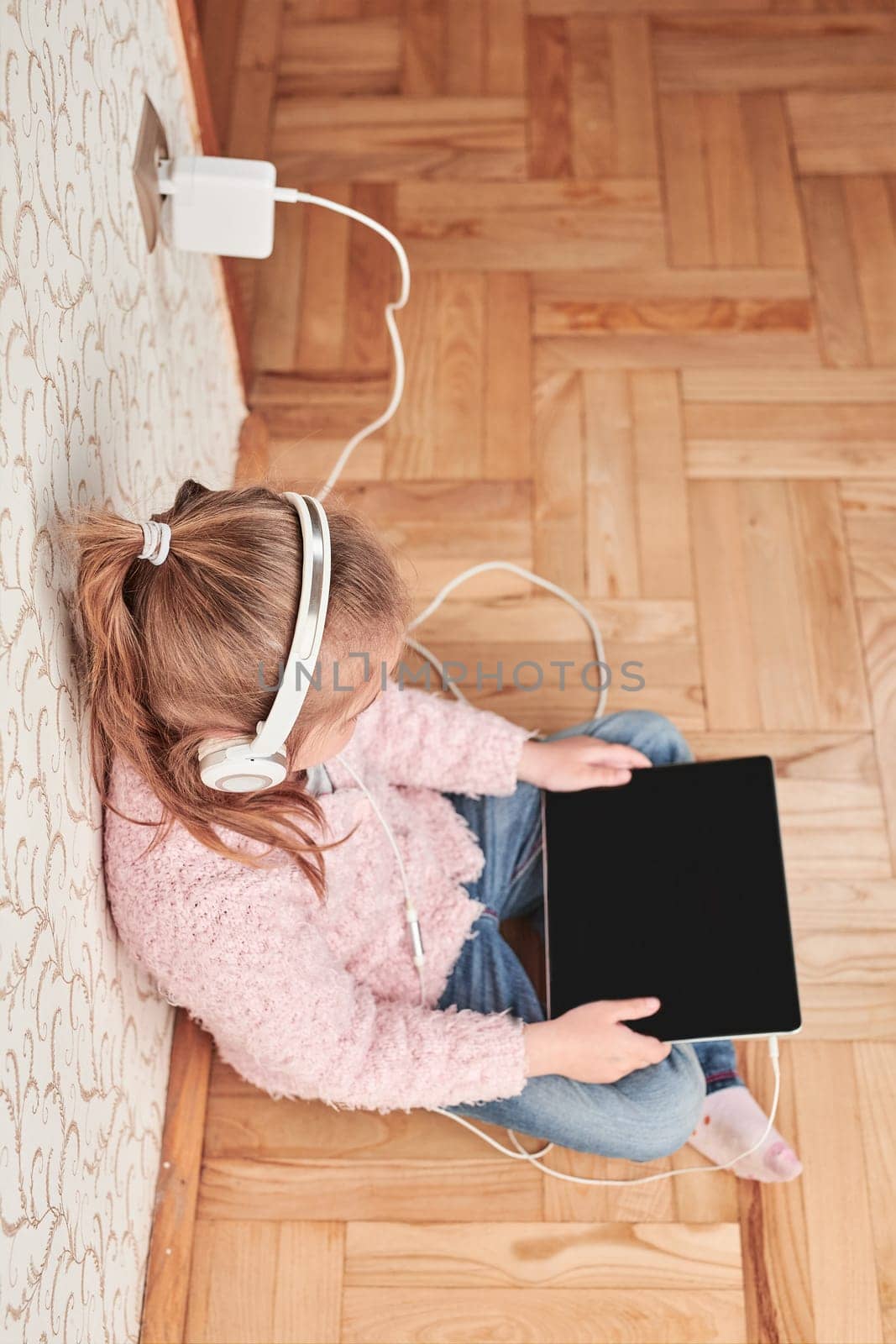 Little girl preschooler learning online solving puzzles playing educational games listetning to music and sounds using tablet and headpphones at home during pandemic quarantine