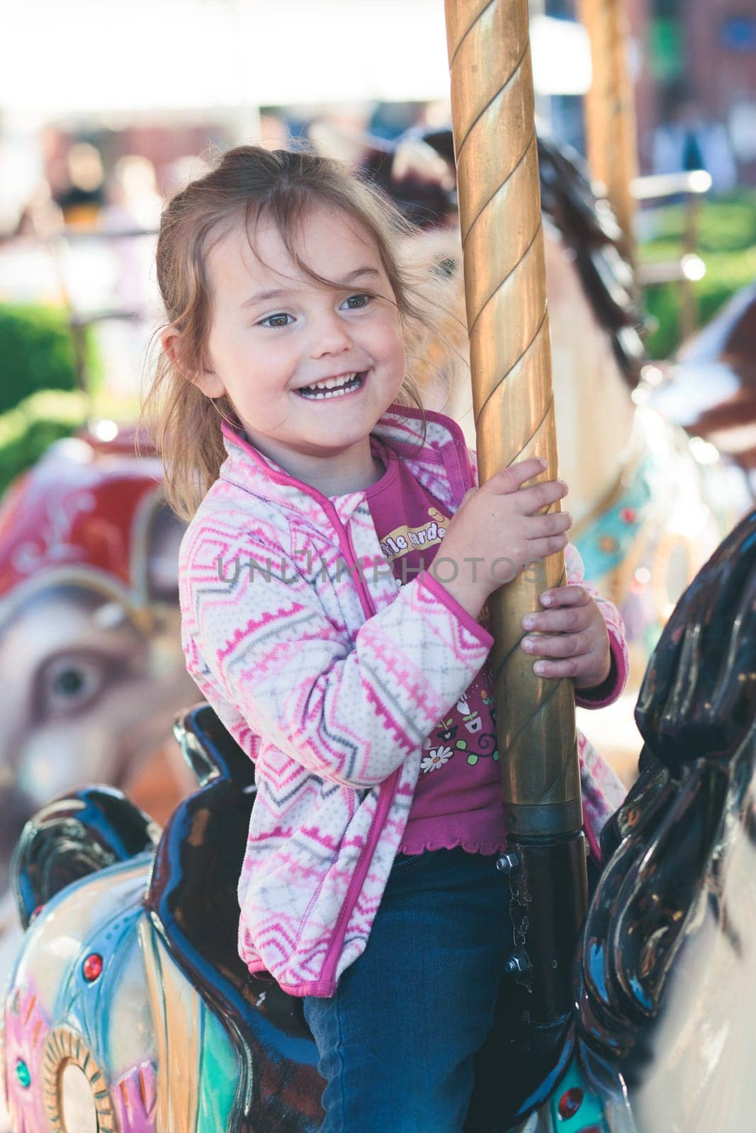 Little adorable smiling girl riding a horse on roundabout carousel at funfair