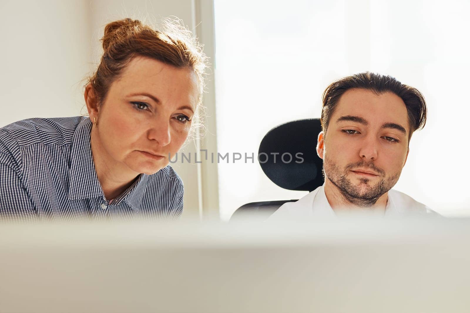 Two business people discussing financial data looking at computer screen. Businesswoman talking to young male coworker in office. People entrepreneurs having conversation working together. Workmates talking about project