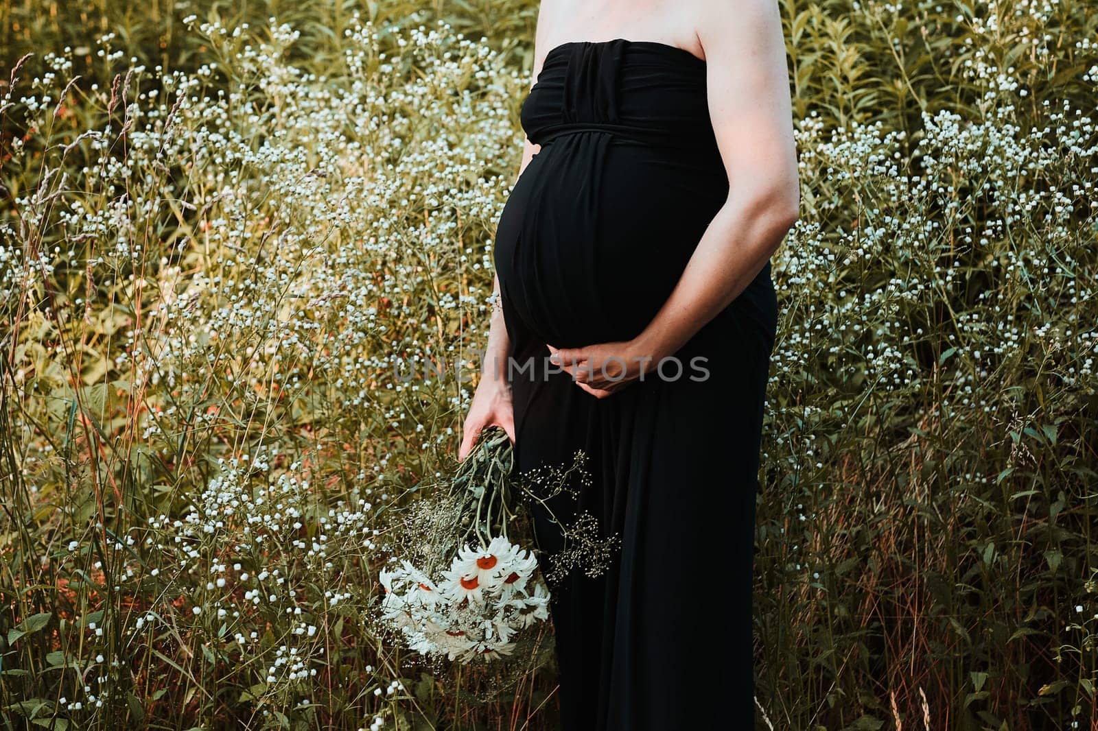 Pregnant woman hugging her tummy standing outdoors surrounded by nature. Pregnancy, expectation, motherhood concept
