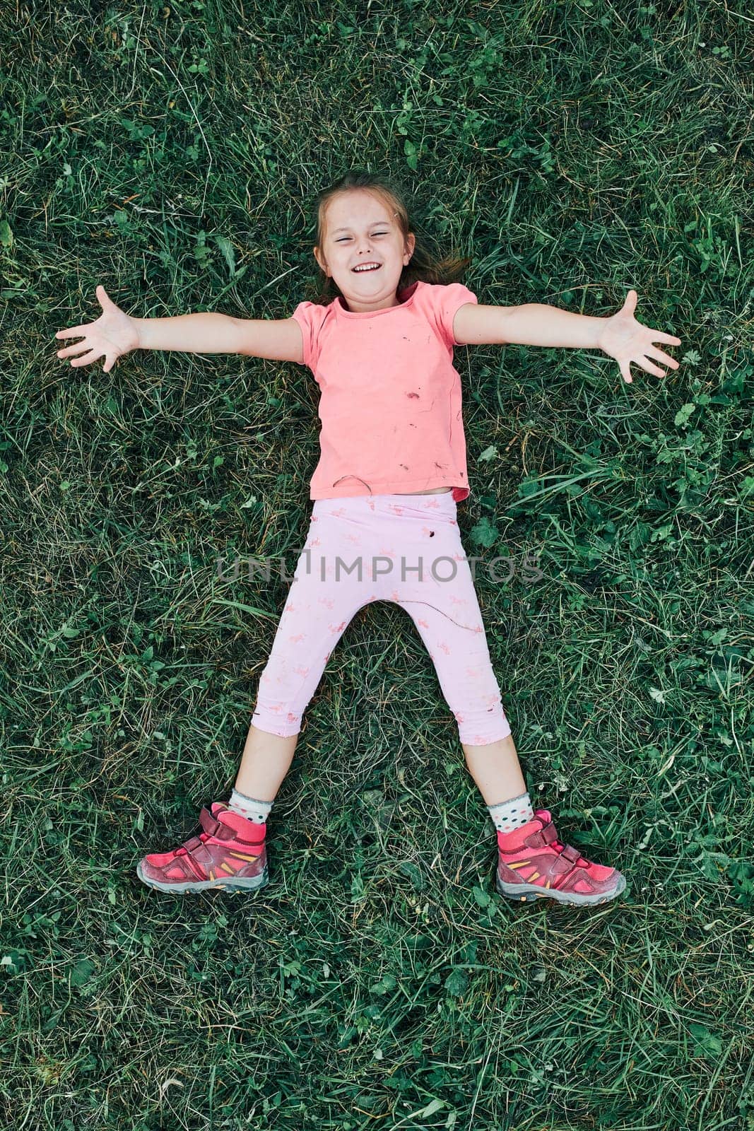 Little girl laying playing on grass enjoying summer day. Happy child playing in the field during weekend trip