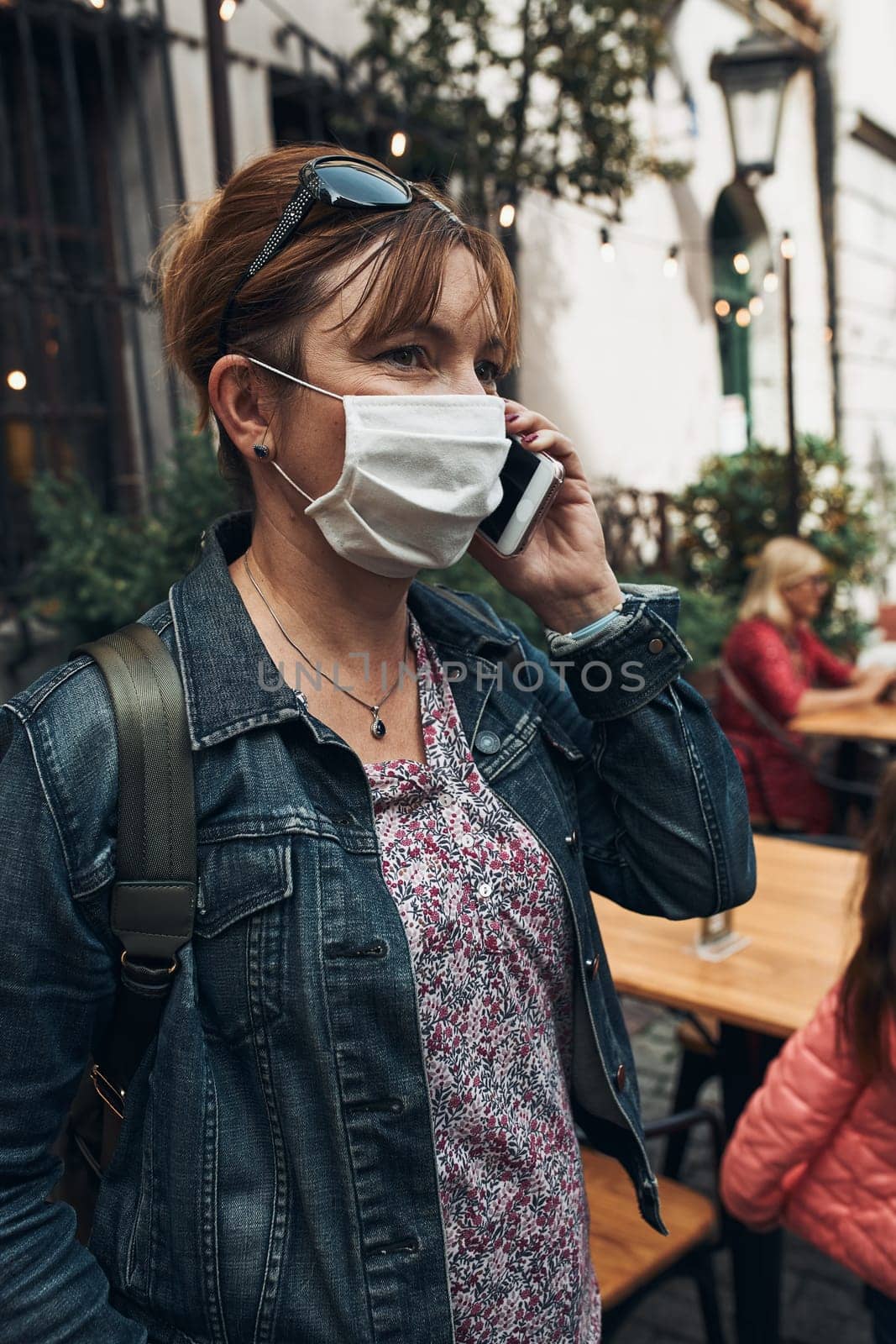 Young woman talking on phone standing in a street downtown. Woman is wearing the face mask to avoid virus infection and to prevent the spread of disease in time of coronavirus