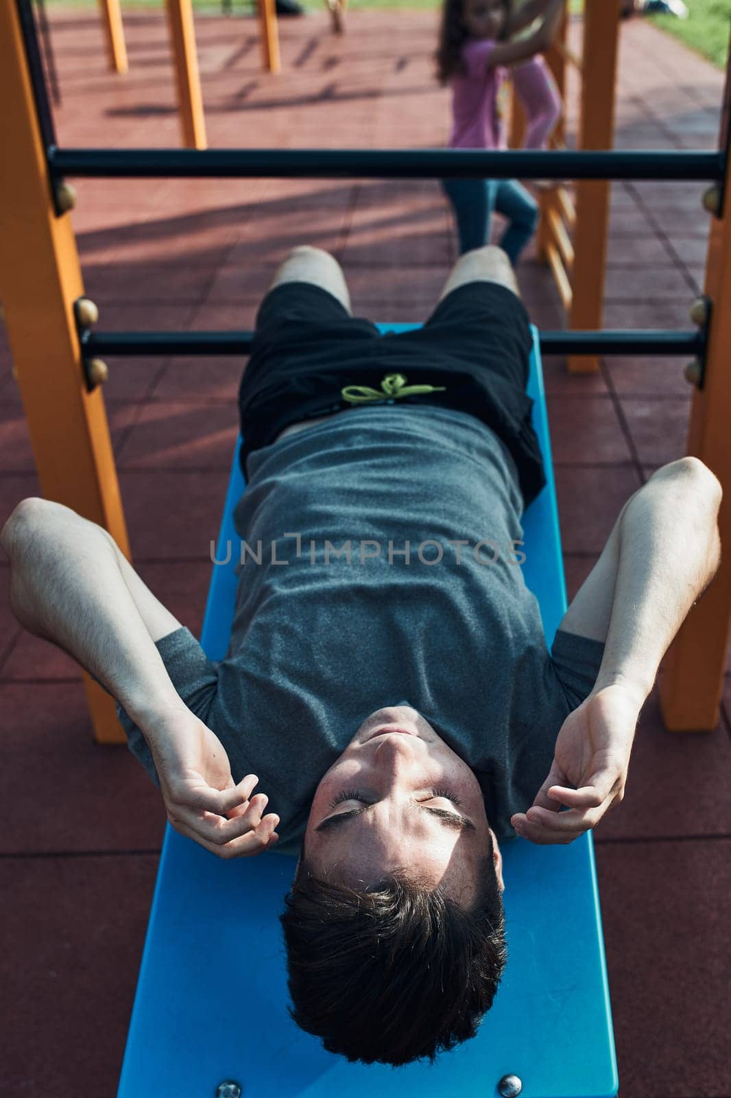 Young man doing sit-ups during his workout in a modern calisthenics street workout park. Man sitting on a sit-up board wearing sportswear