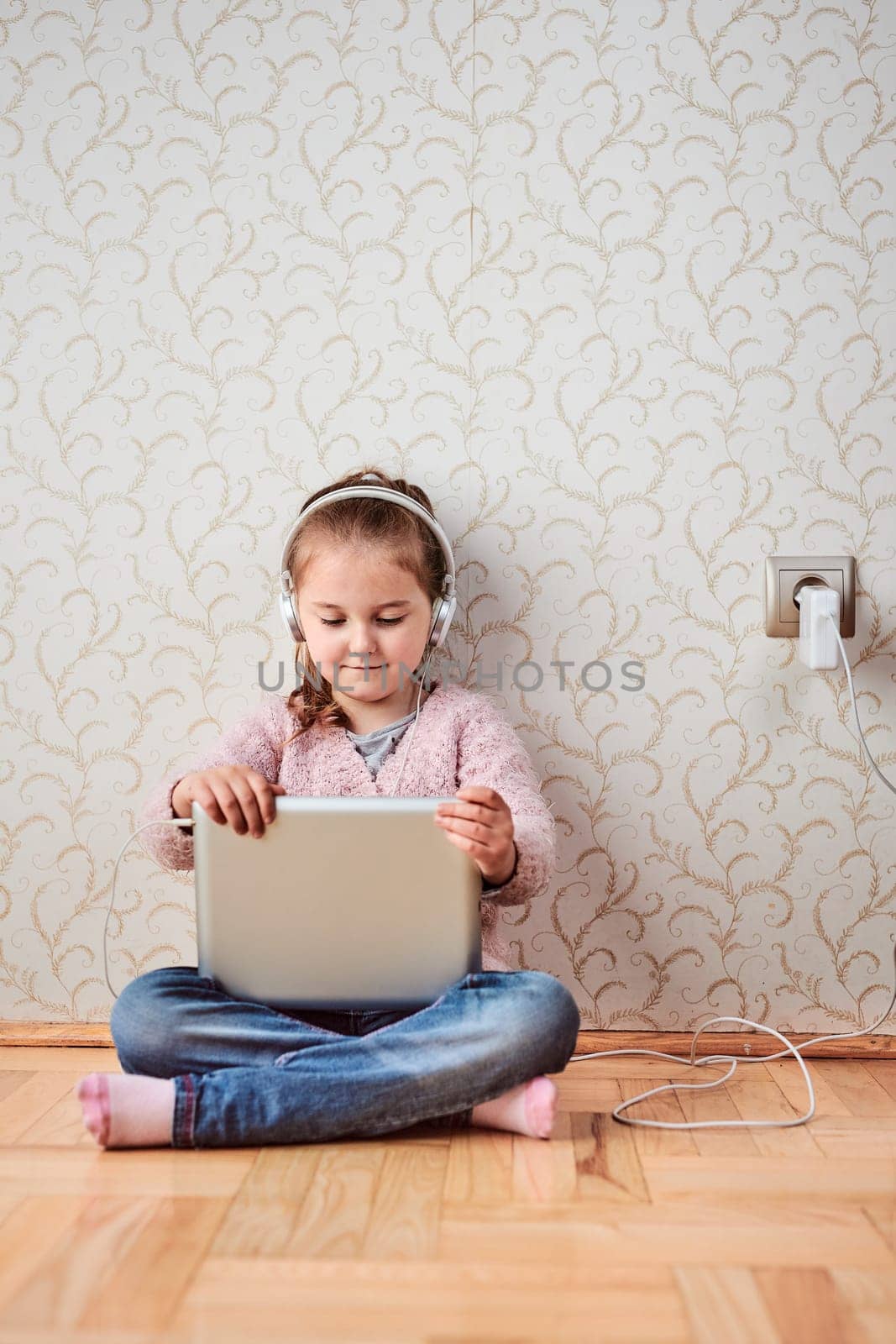 Little girl preschooler learning online solving puzzles playing educational games listetning to music and sounds using tablet and headpphones at home during pandemic quarantine