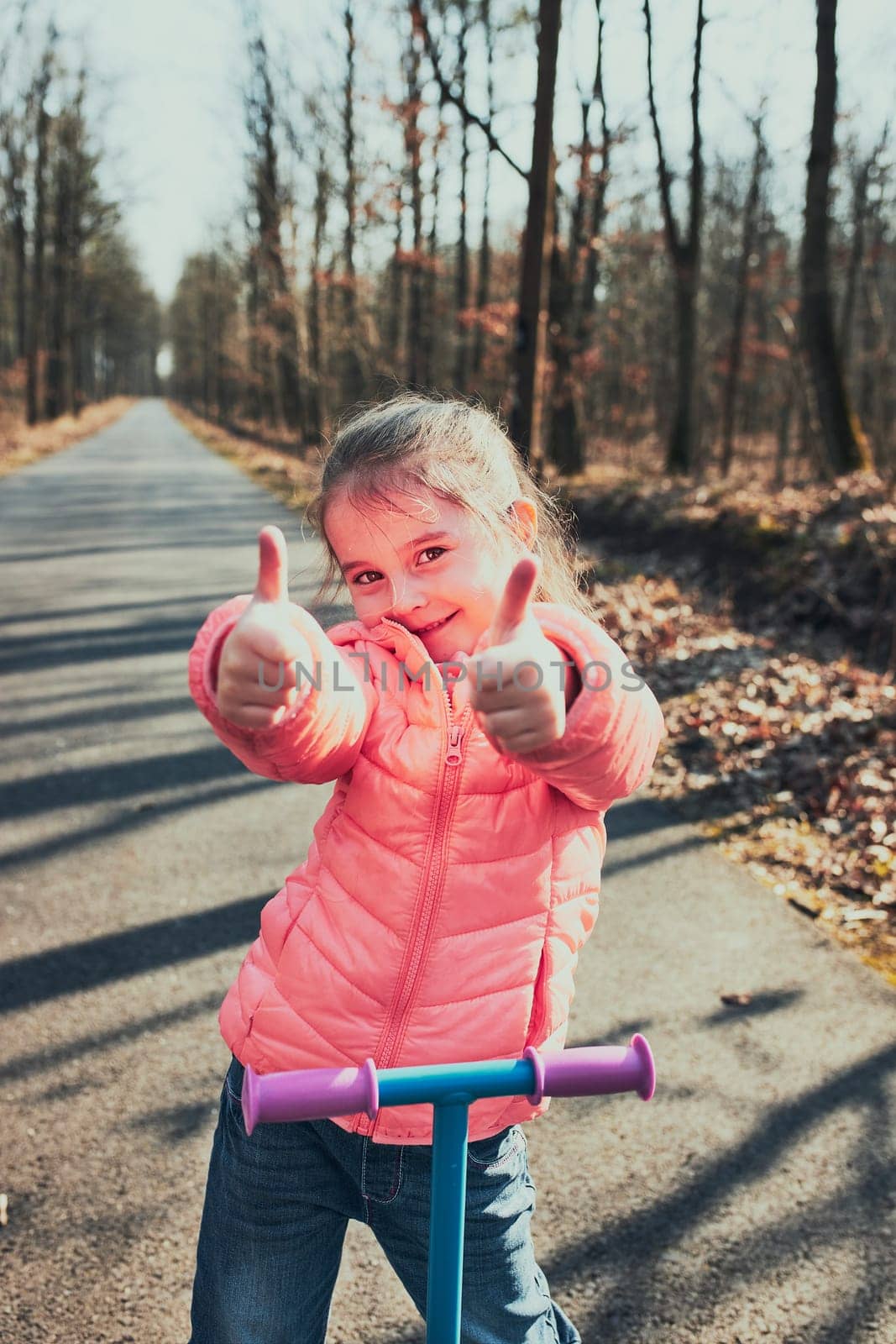 Little girl playing in the park, riding a scooter, having fun on sunny autumn day. Real people, authentic situations