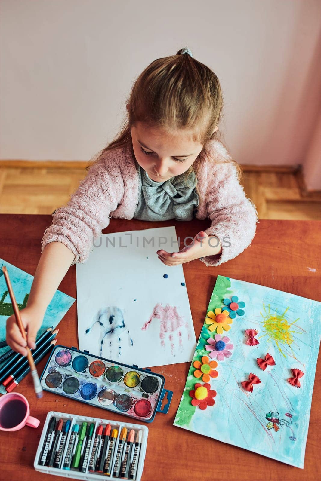 Little girl preschooler painting a picture using colorful paints and crayons. Child having fun making a picture during an art class in the classroom