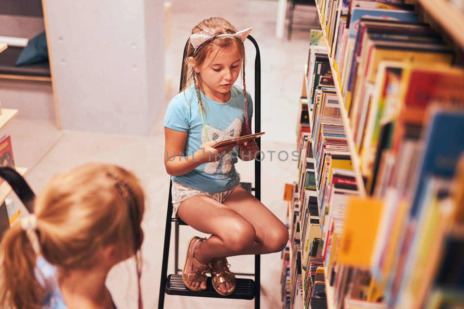 Schoolgirls looking for audio books in school library. Students choosing set books. Elementary education. Doing homework. Learning from books. Back to school