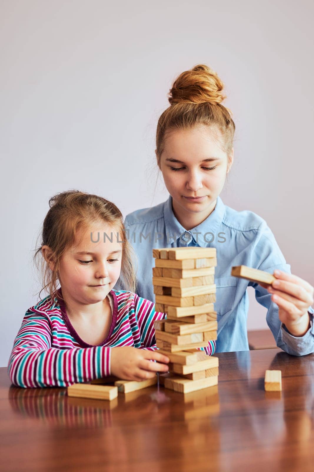 Little girl preschooler and her elder sister playing together with wooden blocks game toy. Siblings spending time sitting at desk at home