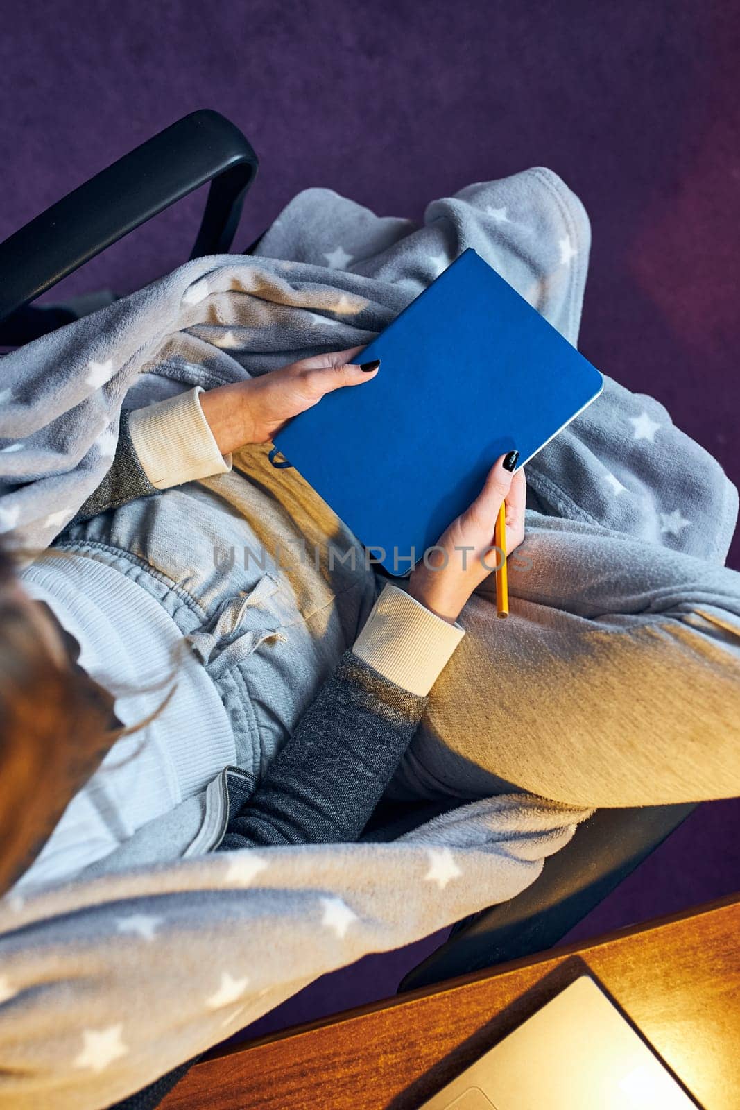 Young woman holding diary, writing in journal. Making notes in diary sitting in chair at home