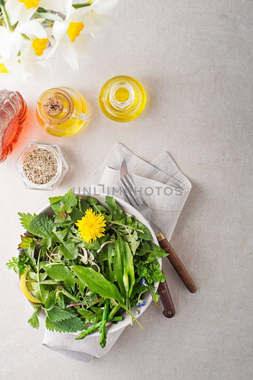 Healthy salad with spring plants and herbs. Dandelion, wild garlic, asparagus, flowers and nettle om bright table background