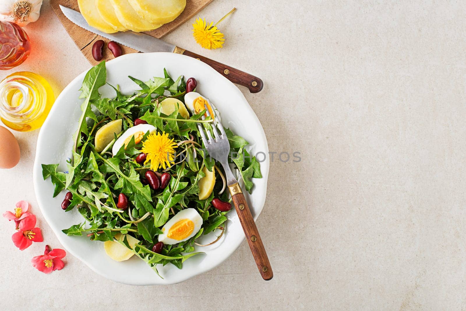 Dandelion salad with eggs, potato and beans on bright table background closeup