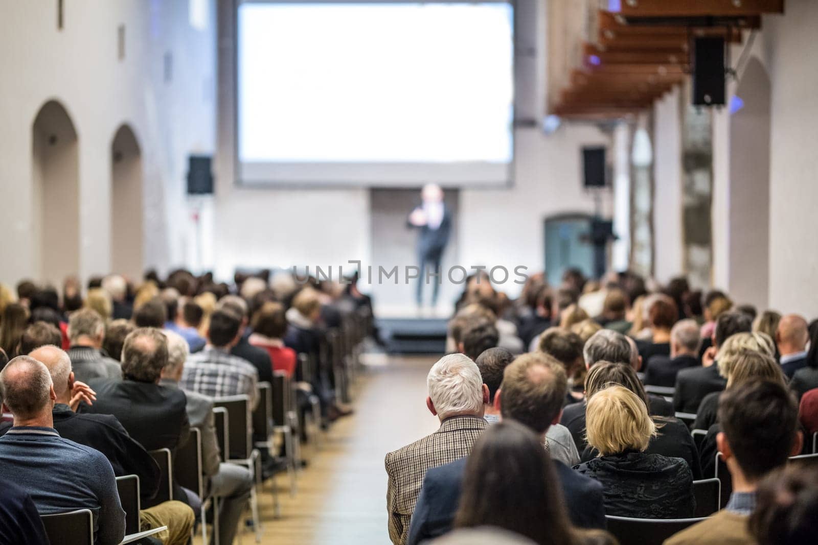 Speaker giving a talk in conference hall at business event. Audience at the conference hall. Business and Entrepreneurship concept. Focus on unrecognizable man in the audience.