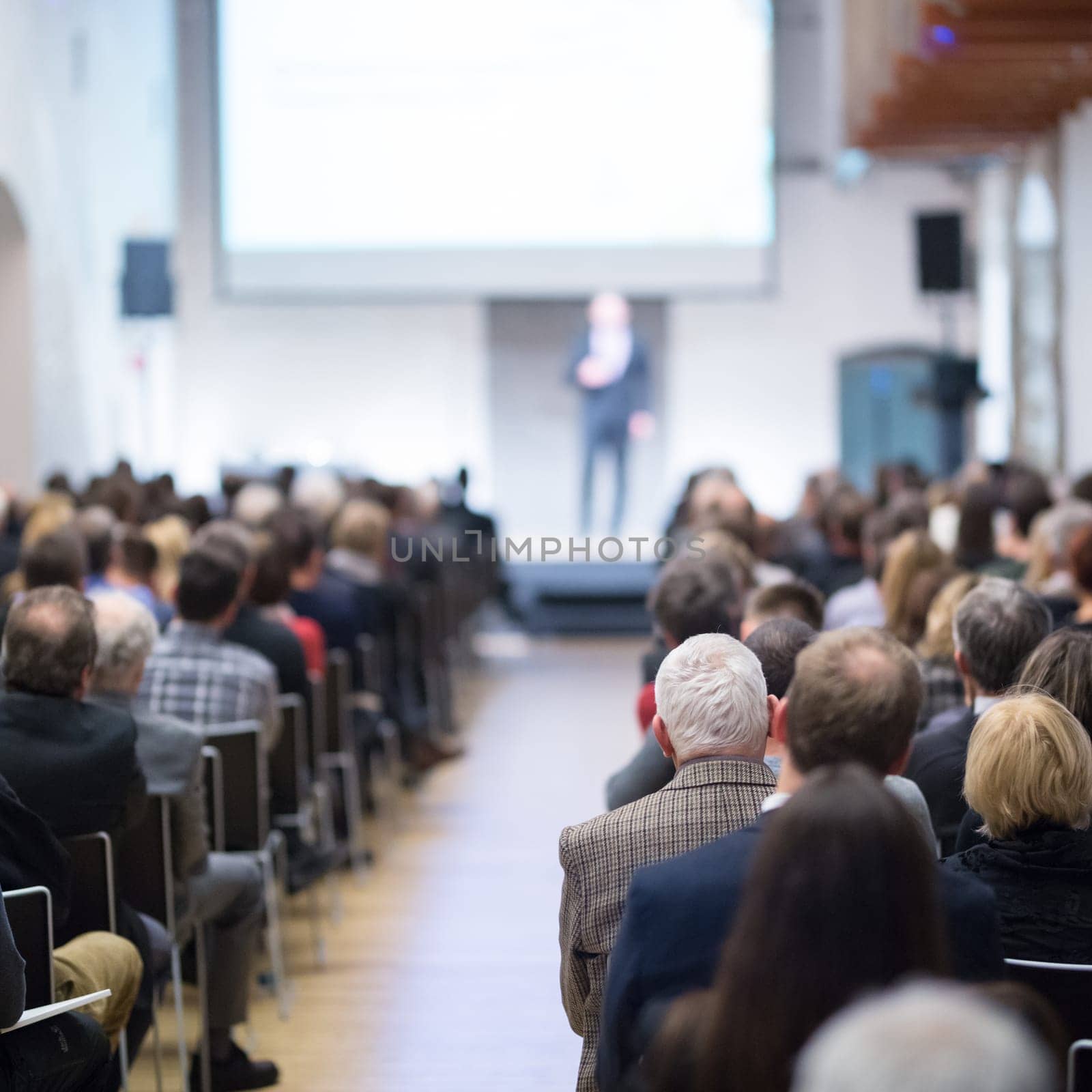 Speaker giving a talk in conference hall at business event. Audience at the conference hall. Business and Entrepreneurship concept. Focus on unrecognizable businessman in the audience.