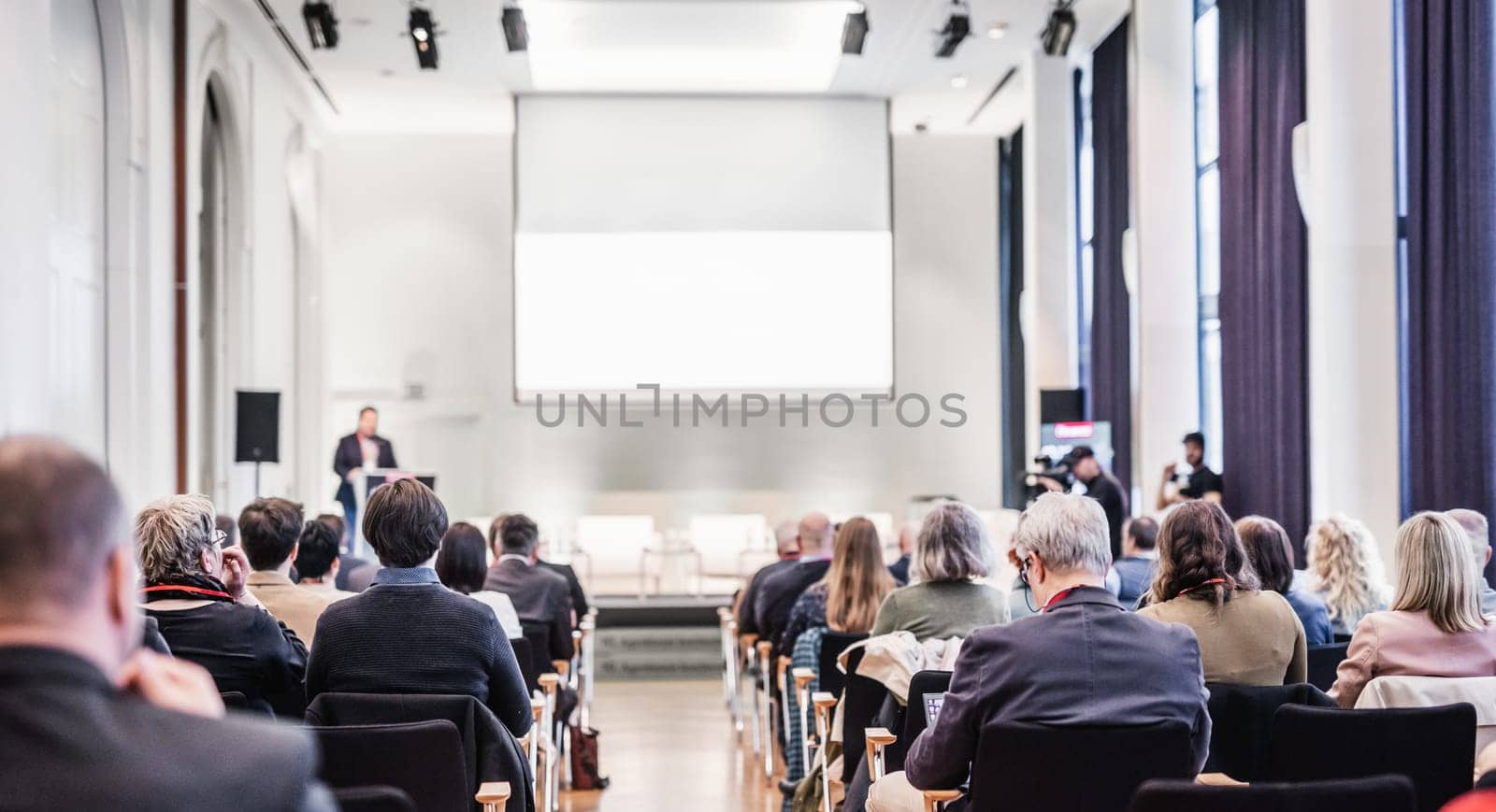 Speaker giving a talk in conference hall at business event. Rear view of unrecognizable people in audience at the conference hall. Business and entrepreneurship concept