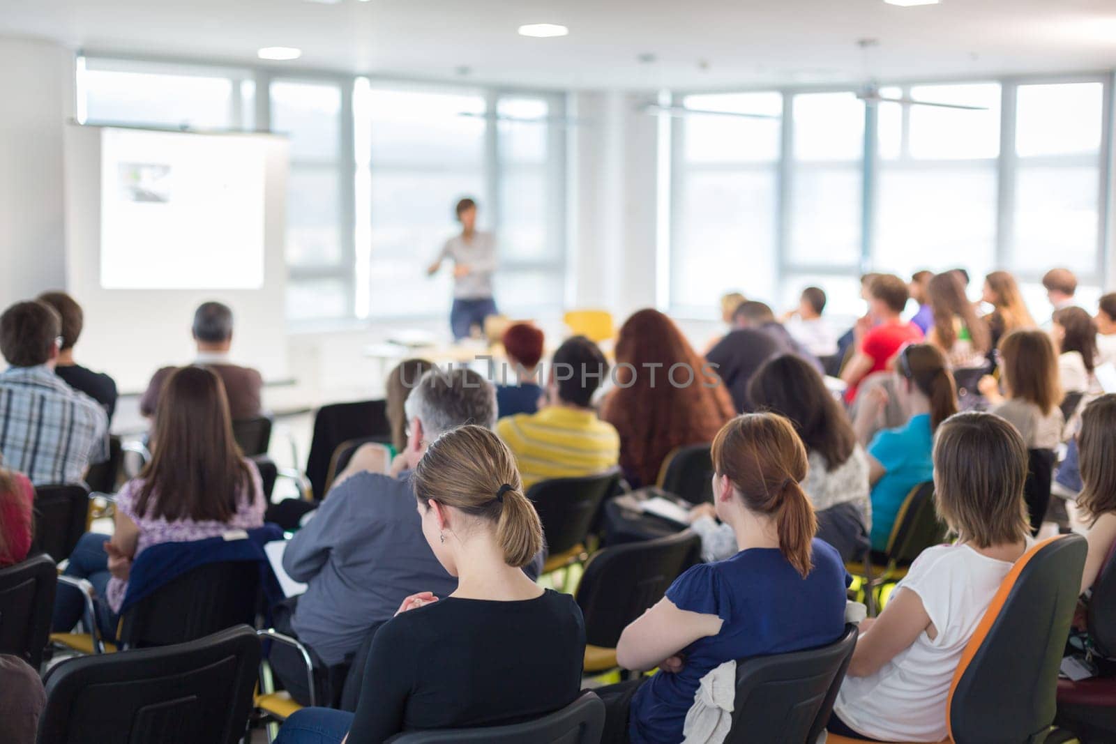 Business and entrepreneurship symposium. Speaker giving a talk at business meeting. Audience in conference hall. Rear view of unrecognized participant in audience.