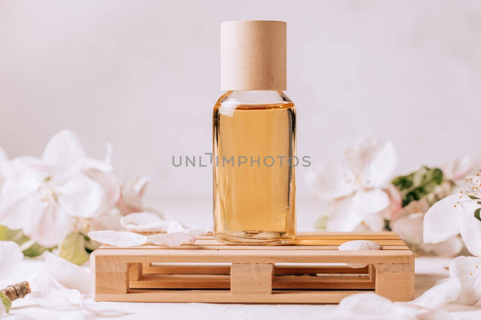 Cosmetic, aroma or massage oil on wooden podium in form of pallet on light plaster surface with apple flowers