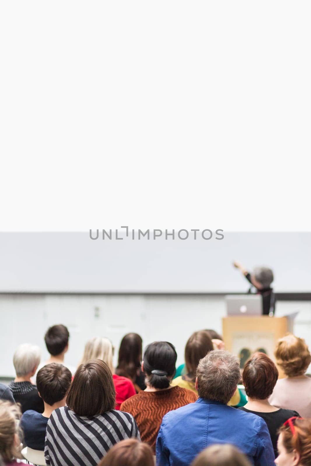 Business and entrepreneurship symposium. Female speaker giving a talk at business meeting. Audience in conference hall. Rear view of unrecognized participant in audience. Copy space on whitescreen.