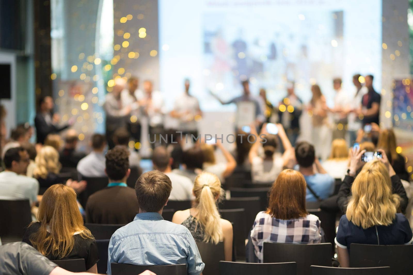 Young business team receiving award prize at best business project competition event. Business and entrepreneurship award ceremony theme. Focus on unrecognizable people in audience.