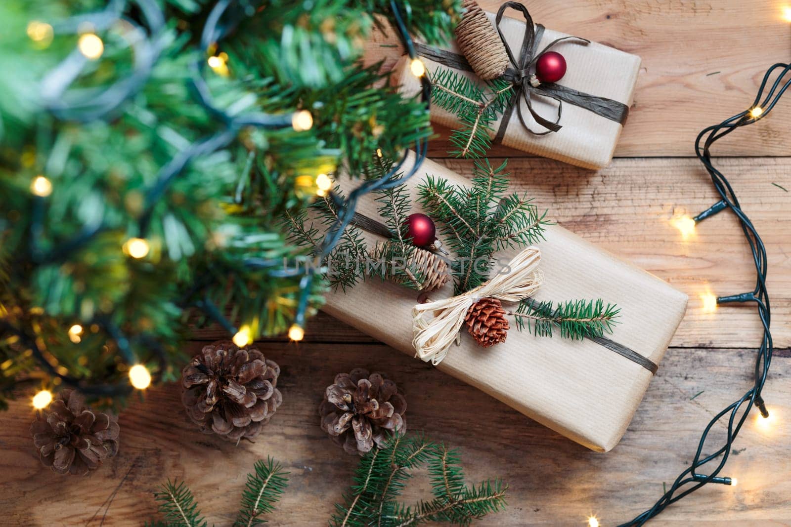 Christmas presents under a Christmas tree. Gifts wrapped in paper decorated with cones and pine twigs put on wooden floor. View from above. Copy space for text at top of image