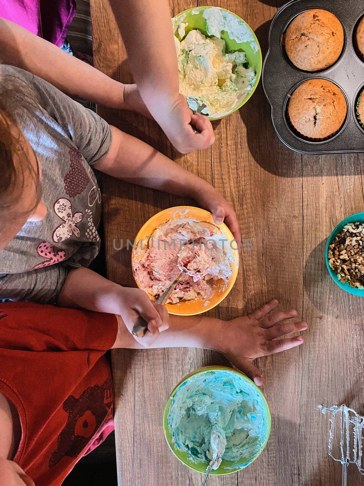 Group of children baking cupcakes, preparing ingredients, toppings, sprinkles for decorating cookies. Kids learning to cook, working together in kitchen at home. Concept of happy family