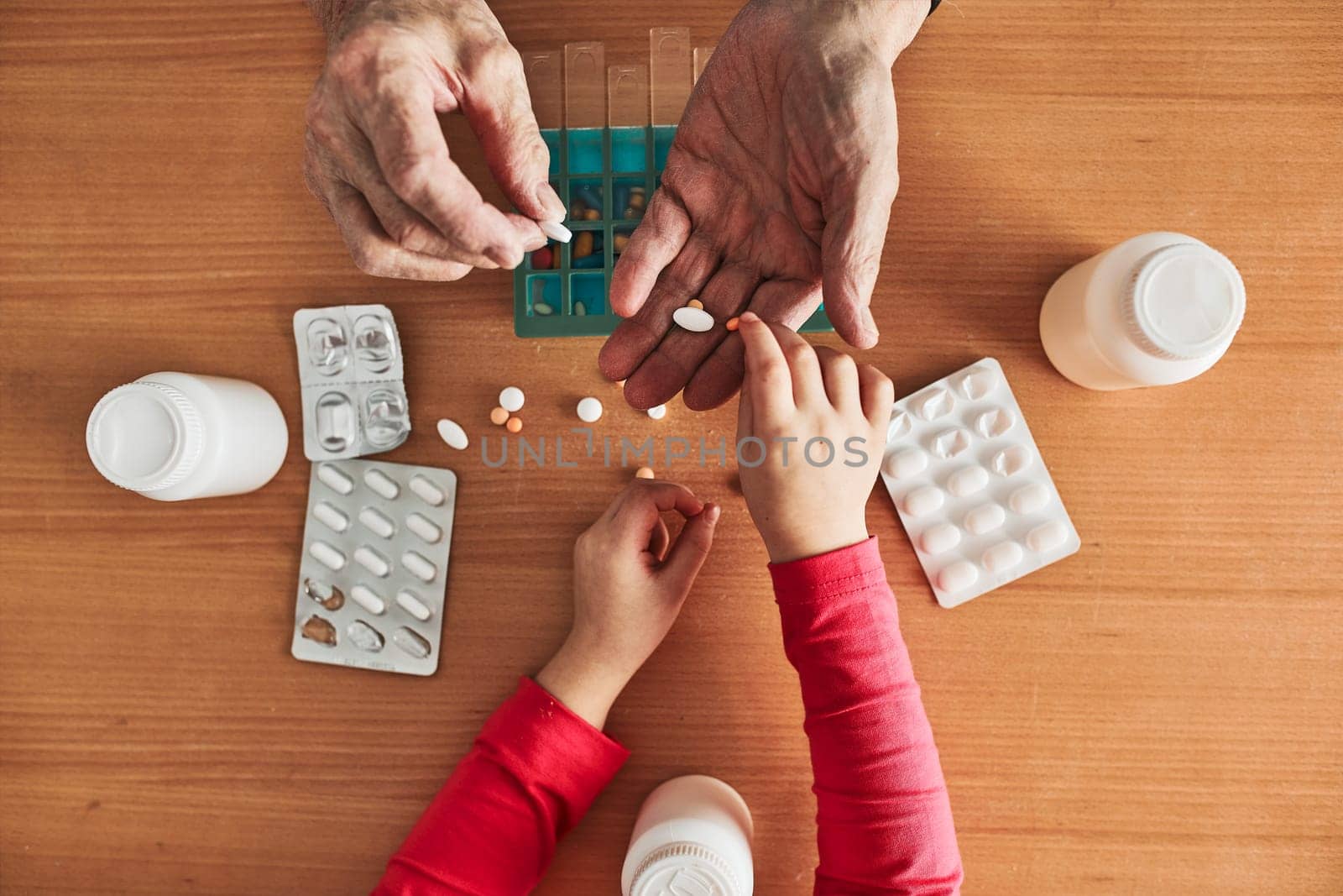 Grandchild helping grandfather to organize medication into pill dispenser. Senior man taking pills from box. Healthcare and old age concept with medicines. Medicaments on table