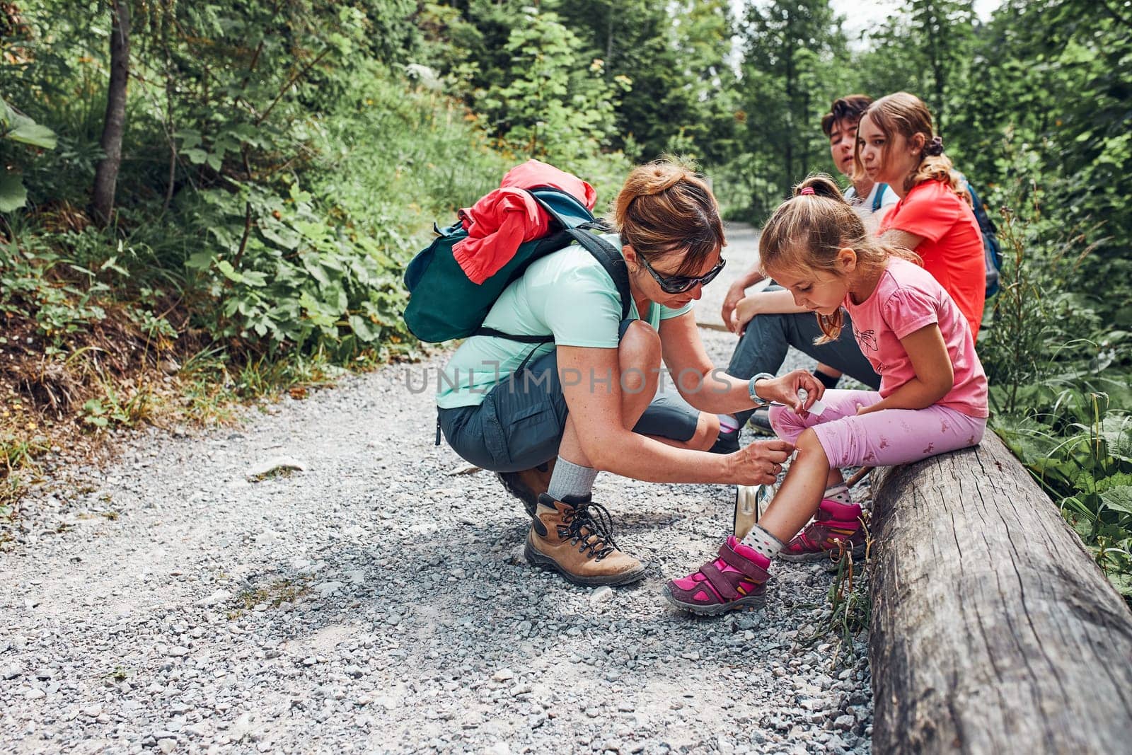 Mother dressing the wound on her little daughter's knee with medicine in spray. Accident happened during family summer vacation trip. People actively spending time