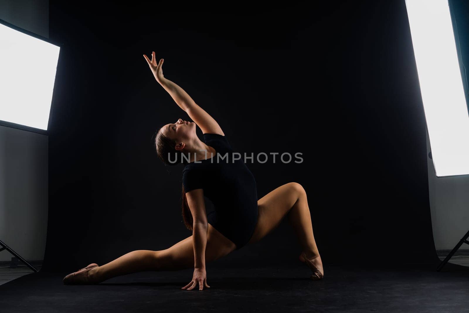 A girl gymnast in a swimsuit does tricks on white and dark background. Front view